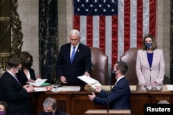 FILE - U.S. Vice President Mike Pence hands the West Virginia certification to staff as Speaker of the House Nancy Pelosi (D-CA) listens during a joint session of Congress after working through the night, at the Capitol in Washington, Jan. 7, 2021.