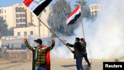 伊拉克民兵和支持者在美國駐巴格達大使館保安人員發射的催淚彈煙霧中揮動伊拉克旗幟。（2020年1月1日） 