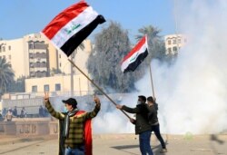 Para pengunjuk rasa dan pejuang milisi mengibarkan bendera Irak di dekat gas air mata yang dilemparkan oleh petugas keamanan Kedubes AS, selama protes untuk mengutuk serangan udara di pangkalan milik Hashd al-Shaabi. (Foto: Reuters)