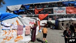 FILE —A woman hangs out laundered clothes to dry outside a tent inscribed with greeting messages for the Muslim holy month of Ramadan, at a camp sheltering displaced Palestinians erected in a school run by UNRWA for Palestine Refugees in Rafah.