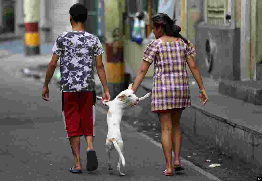 Warga Filipina berjalan dengan anjing mereka di kota Intramuros di Manila, Filipina.