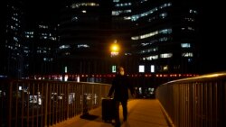 A man wearing a face mask to protect against the spread of the coronavirus wheels a suitcase across a pedestrian bridge in Beijing, Wednesday, Jan. 13, 2021.