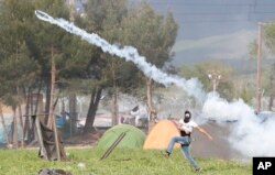 A migrant man throws a can of the tear gas back toward Macedonian police during a protest at the northern Greek border point of Idomeni, Greece, April 10, 2016.
