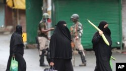 Kashmiri women carry bags filled with essentials past Indian paramilitary soldiers closing off a street in Srinagar, Indian-controlled Kashmir, Aug. 10, 2019.