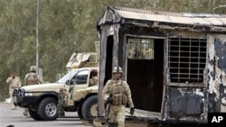 Iraqi army soldiers stand guard near burned trailers at Camp Ashraf north of Baghdad, Iraq, April 8, 2011