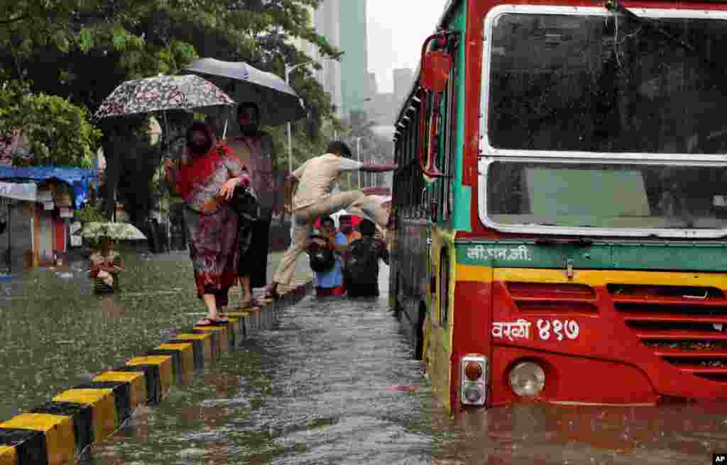 A man tries to climb into a bus from a road median on a water-logged street during heavy rains in Mumbai, India.