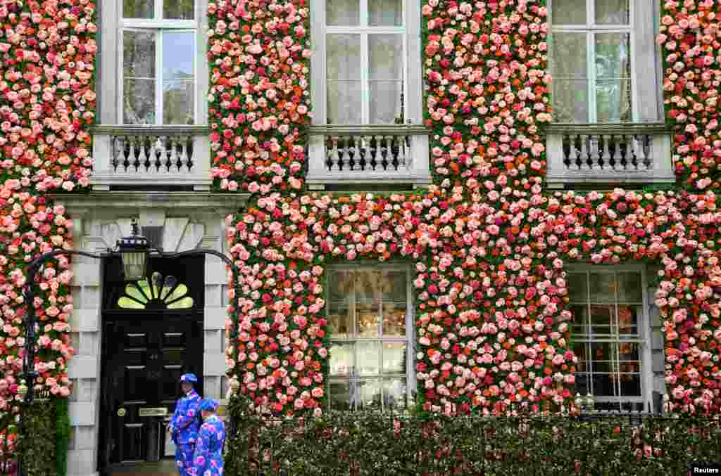 Doormen dressed in floral patterned suits stand on duty outside of a private club with it&#39;s front covered in flowers in London.