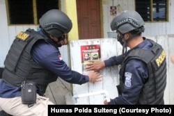 Petugas menempel poster memuat foto dan identitas empat teroris anggota MIT yang masih diburu dalam operasi Madago Raya. Sabtu (25/9/2021). (Foto: Courtesy/Humas Polda Sulteng)