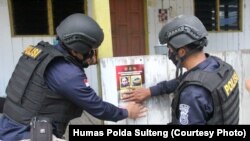 Petugas menempel poster memuat foto dan identitas empat teroris anggota MIT yang masih diburu dalam operasi Madago Raya di sejumlah wilayah di Sulawesi Tengah, pada 25 September 2021. (Foto: Courtesy/Humas Polda Sulteng)