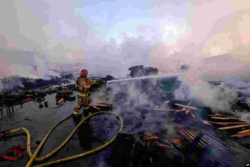 A firefighter battles a fire at a commercial yard in Compton, California. A huge fire visible across Los Angeles burned material in a commercial yard and parked buses.