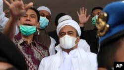 Rizieq Shihab (tengah), dikawal oleh polisi dan kuasa hukumnya, tiba di Polda Metro Jaya, Sabtu, 12 Desember 2020. (Foto: AP)