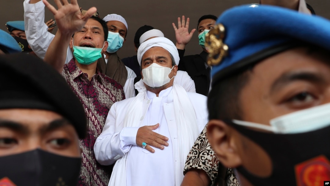 Rizieq Shihab (tengah), dikawal oleh polisi dan kuasa hukumnya, tiba di Polda Metro Jaya, Sabtu, 12 Desember 2020. (Foto: AP)
