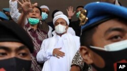 Rizieq Shihab (tengah), dikawal oleh polisi dan kuasa hukumnya, tiba di Polda Metro Jaya, Sabtu, 12 Desember 2020. (Foto: AP)