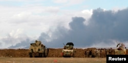 FILE - Iraqi soldiers gather near vehicles as smoke rises from oil wells in the Ajil field east of Tikrit in the Salahuddin province that were set on fire by Islamic State militants in March 2015.