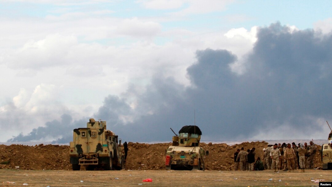 Iraqi soldiers gather near vehicles as smoke rises from oil wells in the Ajil field east of Tikrit in the Salahuddin province that were set on fire by Islamic State militants, March 4, 2015. 