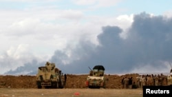 Iraqi soldiers gather near vehicles as smoke rises from oil wells in the Ajil field east of Tikrit in the Salahuddin province that were set on fire by Islamic State militants, March 4, 2015. 