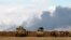 Iraqi soldiers gather near vehicles as smoke rises from oil wells in the Ajil field east of Tikrit in the Salahuddin province that were set on fire by Islamic State militants, March 4, 2015. 