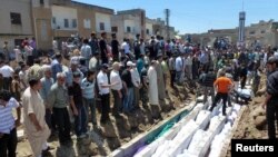 La gente se reúne alrededor de los cádaveres de las víctimas de un bombardeo de las fuerzas sirias en Houla, en el que murieron 108 personas. Decenas más habrían muerto este lunes en nuevos ataques.