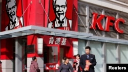 FILE - A man holds instant noodle packs in front of a KFC restaurant in Beijing.