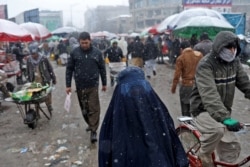 FILE - An Afghan woman walks on the street during a snowfall in Kabul, Jan. 3, 2022.