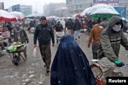 FILE - An Afghan woman walks on the street during a snowfall in Kabul, Jan. 3, 2022.