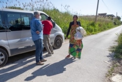 FILE - In this photo taken on April 27, 2020, father Daniele Moschetti talks with Mercy Fred, a woman from Nigeria, after she received two bags with food in Castel Volturno, near Naples, Southern Italy.