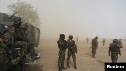 FILE - Cameroonian soldiers from the Rapid Intervention Brigade stand guard amidst dust kicked up by a helicopter in Kolofata, Cameroon, March 16, 2016.