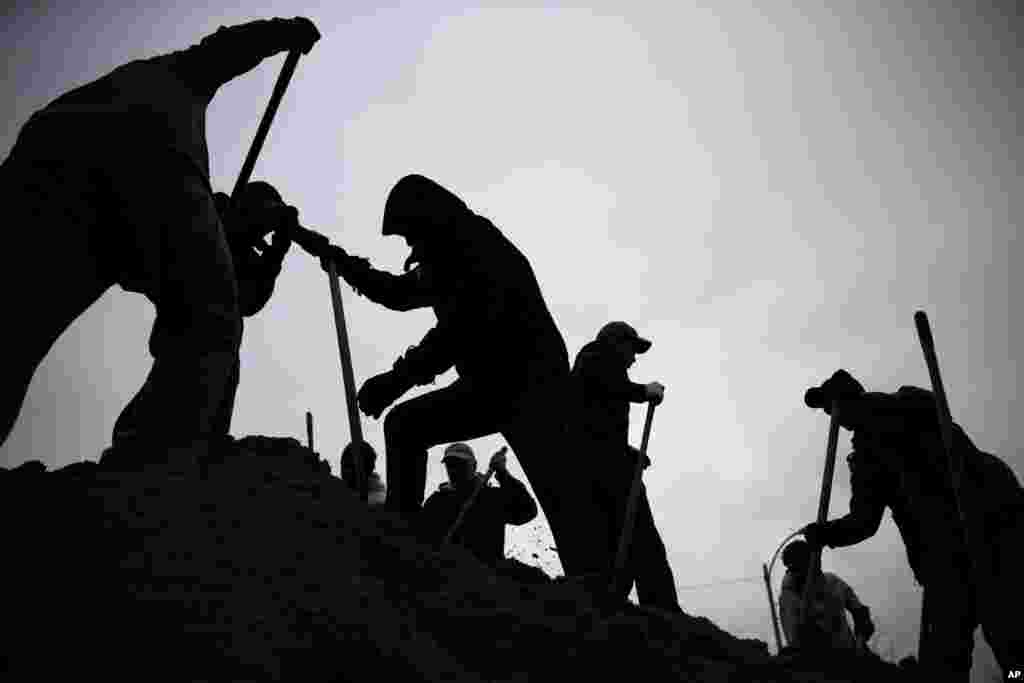 Against a gray winter sky, volunteers use shovels atop a pile of sand as they help fill sandbags in St. Louis, Missouri, USA.