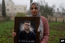 Mona, 36, mother of Tawfic Abdel Jabbar, poses with a framed photo of her son at the family's Palestinian home in the West Bank on Jan. 23.