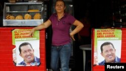 A woman stands in a restaurant between posters of Venezuela's President Hugo Chavez, in front of a military hospital, where Chavez is being treated, in Caracas, February 20, 2013.