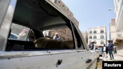 People gather near a car damaged by a mortar shell during fighting between Shi'ite Houthi militants and government forces in Sanaa, Sept. 19, 2014.