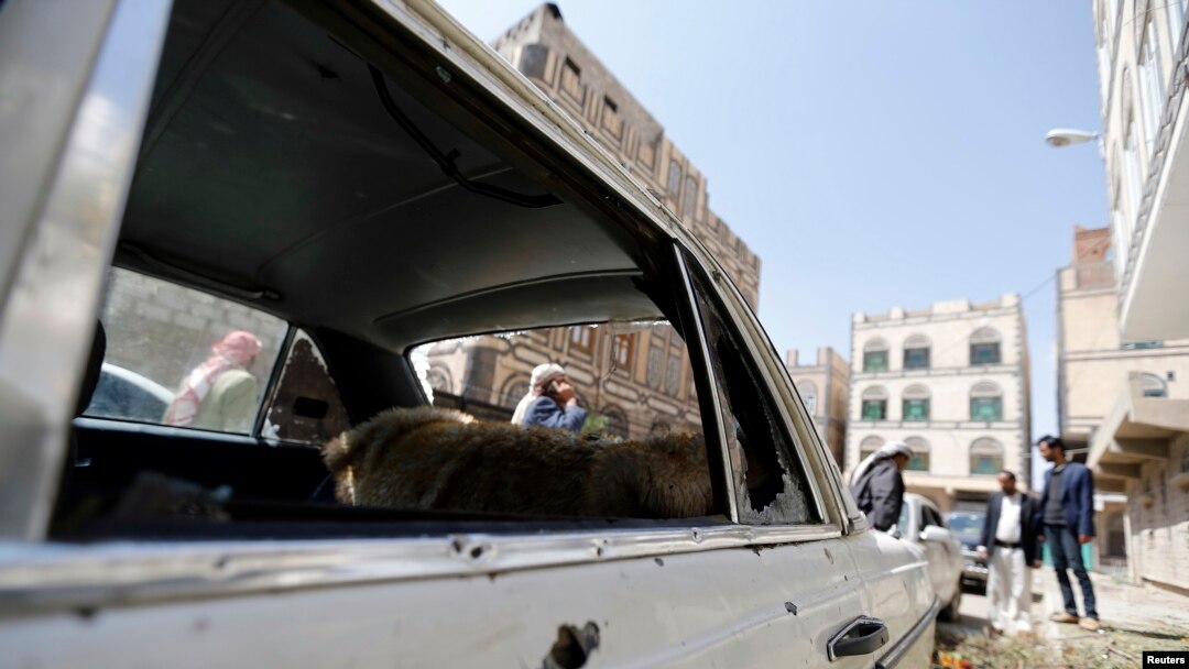 People gather near a car damaged by a mortar shell during fighting between Shi'ite Houthi militants and government forces in Sanaa September 19, 2014. 