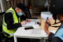 FILE - A man holds up his smartphone to share health app data as a government worker notes down his phone number at a checkpoint in Beijing, China, April 29, 2020.