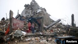 Palestinian children take cover from the rain as they stand atop the ruins of a house, which witnesses said was destroyed by Israeli shelling during the most recent conflict between Israel and Hamas, on a rainy day in the east of Khan Younis in the southe