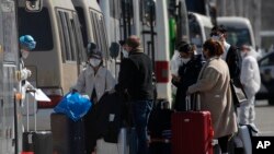 A worker wearing protective gear checks travelers before getting on a bus parked outside the new China International Exhibition Center converted into a transit center for screening oversea arrivals in Beijing, March 17, 2020.