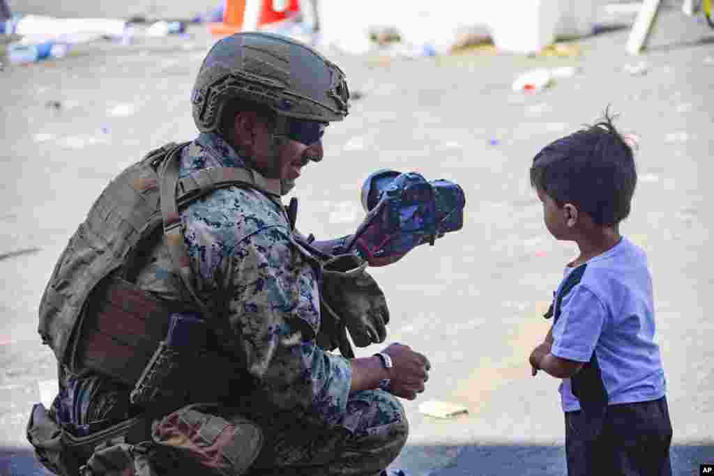 In this image provided by the U.S. Marine Corps, a Marine assigned to the Joint Task Force-Crisis Response shows a child a photograph at Hamid Karzai International Airport in Kabul, Afghanistan, Aug. 28., 2021.