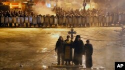 Những tu sĩ Chính thống giáo Ukraine đóng vai trò tích cực trong những cuộc biểu tình ở Kiev. Trong ảnh, một tu sĩ đang cầu nguyện cạnh 2 người biểu tình ủng hộ châu Âu trong một buổi sáng lạnh lẽo, ngày 24 tháng 1, 2014