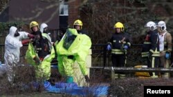 Agentes son ayudados a sacarse los trajes protectores tras reubicar la tienda de campaña forense colocada sobre la banca de Salisbury, Gran Bretaña, donde fueron encontrados un exespía ruso y su hija. Marzo 8 de 2018.