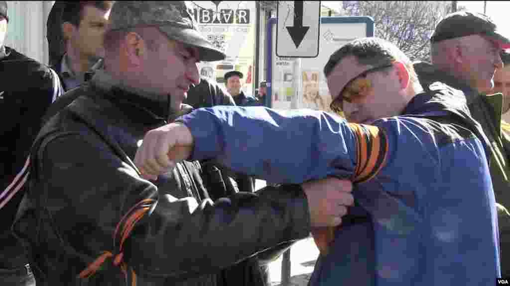 A man attaches a pro-Russian arm band to a another man joining a “Self Defense” group outside parliament in Simferopol, March 3, 2014 (Sebastian Meyer/VOA)