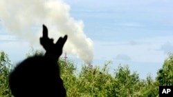 FILE - In this photo taken June 24, 2010, a fruit farmer points to a factory's chimney that blowing smoke from behind a backyard of his home near Map Ta Phut industrial estate in Rayong province, southeastern Thailand.