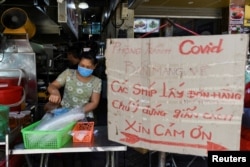 FILE - A woman sells food next to a banner reading "prevent the spread of COVID-19, take away only, please keep your distance 2 meters" amid the coronavirus disease (COVID-19) outbreak in Hanoi, Vietnam, May 31, 2021.