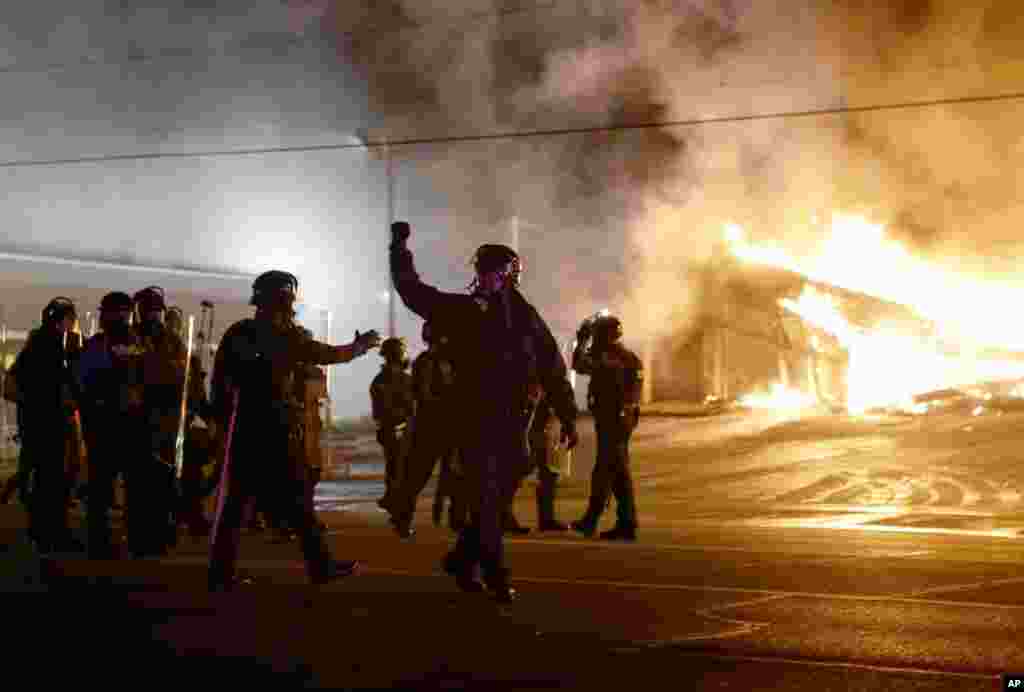 A polícia guarda a área enquanto os populares incendiam alguns edifícios depois do anúncio da decisão do grande júri de que o polícia que atirou fatalmente em Michael Brown Police não será acusado. Ferguson, Missouri, Nov. 24, 2014.