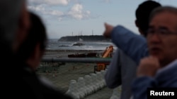Katsumi Miyaguchi, right, deputy mayor of Namie town, points to cranes and chimneys of Tokyo Electric Power Co's tsunami-crippled Fukushima Daiichi nuclear power plant as he guides tourists from Tokyo's universities at an area devastated by the March 11, 2011, earthquake and tsunami.