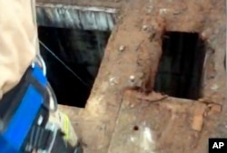 This photo from video provided by the Los Angeles Fire Department shows firefighters dropping a video camera down a large hole next to where a 13-year-old boy fell through through the small hole at right into a river of sewage in the Griffith Park area of