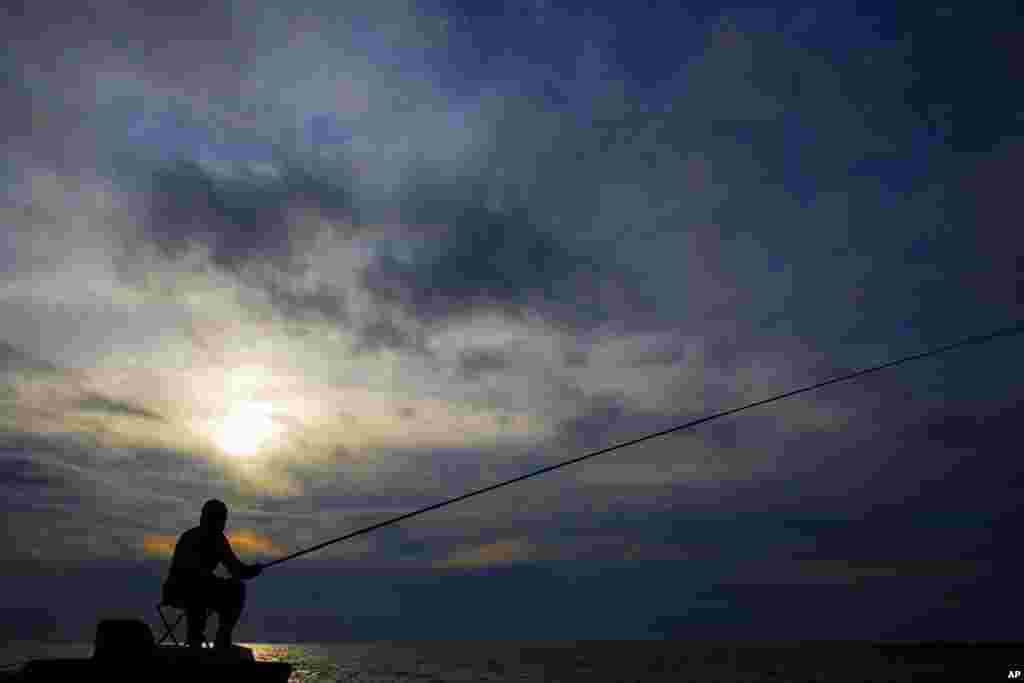 A man casts his fishing pole from a rocky coastal area along the Beirut coastline, Lebanon.
