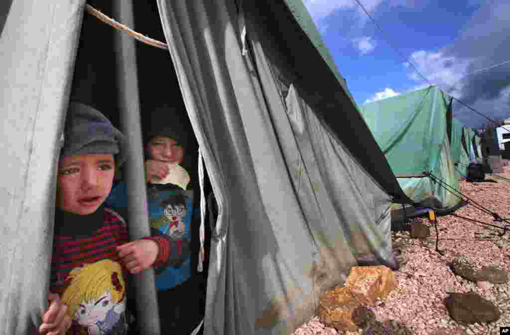 Para bocah lelaki Suriah melongok dari tenda mereka di Marj, Lebanon. (AP/Hussein Malla)