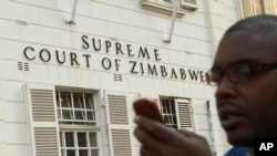 Seorang wartwan tengah memeriksa pesan di telepon genggamnya di depan Mahkamah Agung di Harare, Zimbabwe (9/8).