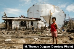 A girl wanders near a typhoon-damaged house and oil tank in the Filipino town of Tanauan in 2013. The Millennium Challenge Corp. supported rehabilitation efforts with the Peace Corps response program.