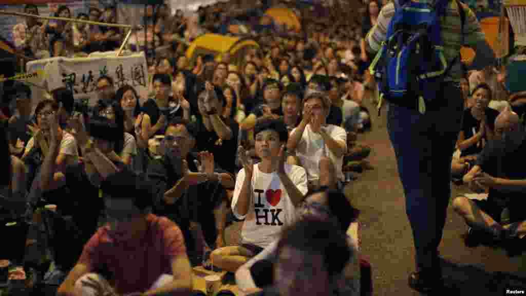 Para demonstran pro-demokrasi bertepuk tangan saat menonton pembicaraan formal antara para pemimpin protes mahasiswa dan pejabat pemerintah dari layar video dekat kantor pusat pemerintahan di Hong Kong (21/10). (Reuters/Carlos Barria) 