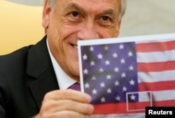 Chilean President Sebastian Pinera holds up a picture of the Chilean flag depicted in the center of the U.S. flag during a meeting with U.S. President Donald Trump in the Oval Office of the White House in Washington, Sept. 28, 2018.